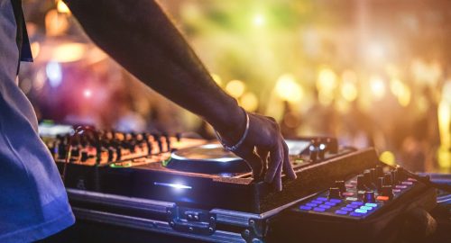 Dj mixing outdoor at beach party festival with crowd of people in background - Summer nightlife view of disco club outside - Soft focus on hand - Fun ,youth,entertainment and fest concept