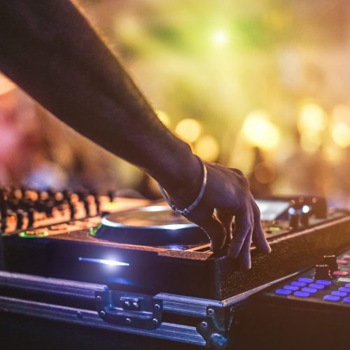 Dj mixing outdoor at beach party festival with crowd of people in background - Summer nightlife view of disco club outside - Soft focus on hand - Fun ,youth,entertainment and fest concept